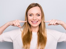 woman smiling while pointing to her teeth 