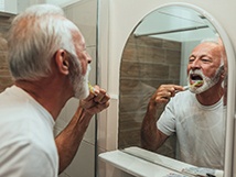 Older man brushing his while looking in the mirror