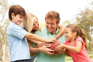 Family Playing American Football Together In Park