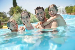 Family smiling in the pool together during a summer day