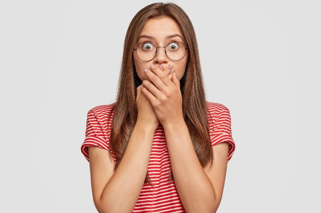 Woman with glasses covering mouth in shock